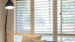 Ein Wohnzimmer mit einer Couch, einer Stehlampe und einem Fenster mit Jalousien.