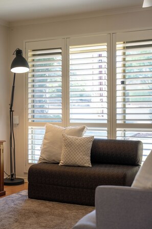 Ein Wohnzimmer mit einer Couch, einer Stehlampe und einem Fenster mit Jalousien.