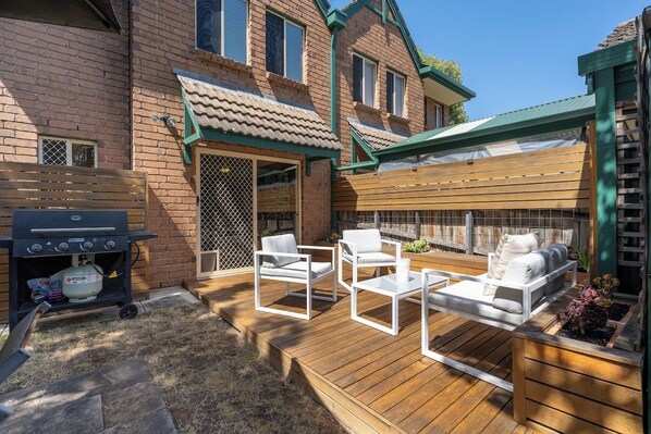 Patio trasero con una parrilla, mobiliario exterior y un área de terraza cubierta.
