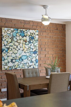 Un comedor con pared de ladrillo, un cuadro de piedras, un ventilador de techo y una planta en maceta.