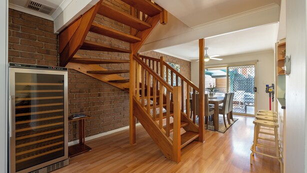 Eine Holztreppe führt zu einer zweiten Etage, einem Küchenbereich mit Kühlschrank und einem Essbereich mit Tisch und Stühlen.