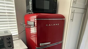 Une cuisine compacte avec un réfrigérateur Galanz rouge, un four à micro-ondes placé sur le dessus, et un petit meuble blanc contenant un grille-pain.