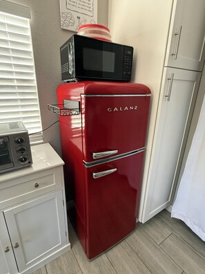 Eine kompakte Küche mit einem roten Galanz-Kühlschrank, einer Mikrowelle darauf und einem kleinen weißen Schrank mit einem Toaster.