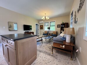 A kitchen with a large island, a dining area with a sofa and chairs, and a living room with a TV and decorative items. - Lovely 1-bedroom MCM apartment with AC near downtown New Bern (New Bern)