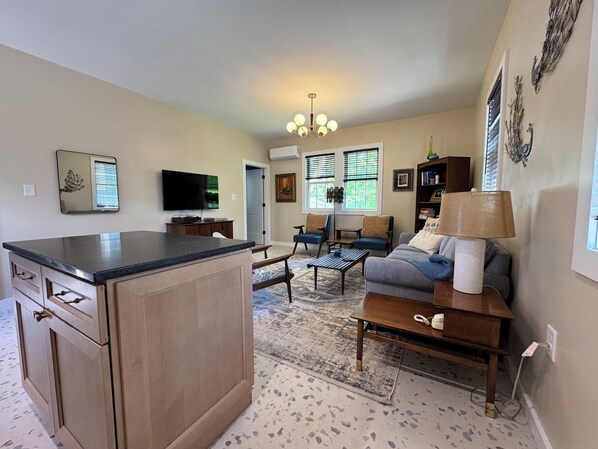 A kitchen with a large island, a dining area with a sofa and chairs, and a living room with a TV and decorative items.