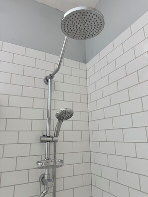 A shower with a handheld showerhead and a wall-mounted rain showerhead in a bathroom with white tiled walls.