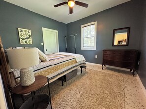 A bedroom with a bed, a dresser, a ceiling fan, a window, and a door.