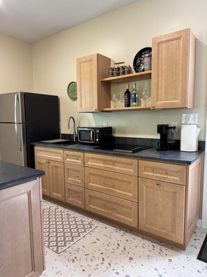 A kitchen with wooden cabinets, a black refrigerator, a microwave, a coffee maker, and a clock on the wall.