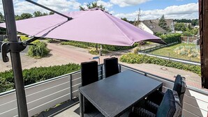 A balcony with a table and chairs, a purple umbrella, and a view of a residential area. - MeerZeit by Interhome (Rehburg)
