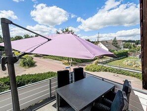 A balcony with a table and chairs, a purple umbrella, and a view of a residential area. - MeerZeit by Interhome (Rehburg)
