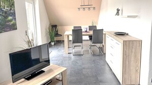 A modern kitchen with a dining area, a TV on a wooden stand, and a ceiling light fixture. - MeerZeit by Interhome (Rehburg)