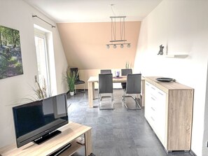 A modern kitchen with a dining area, a TV on a wooden stand, and a ceiling light fixture. - MeerZeit by Interhome (Rehburg)
