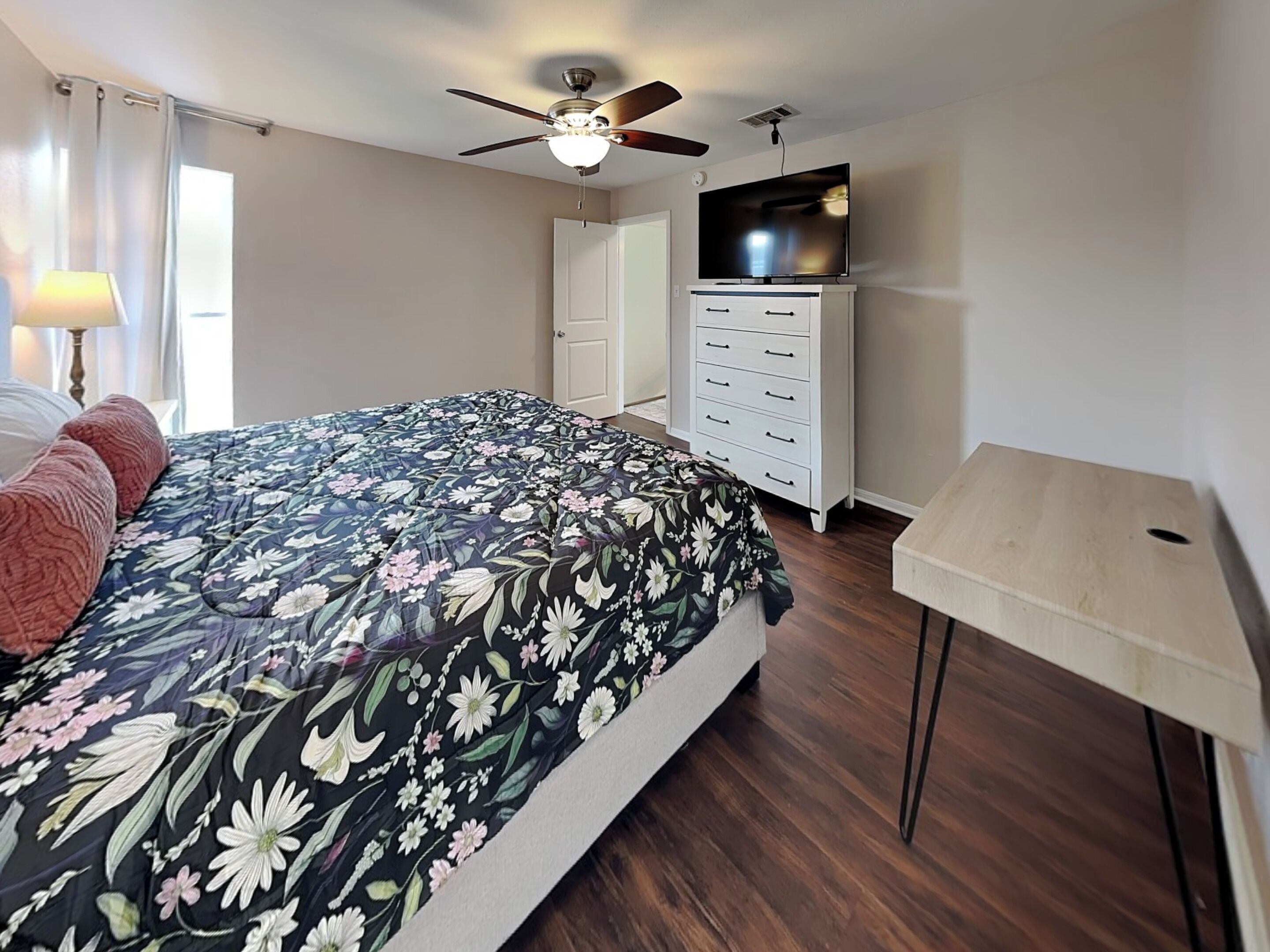 Un dormitorio con una cama, ventilador de techo, televisor, cómoda y lámpara.