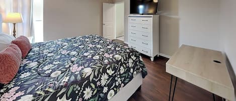 Un dormitorio con una cama, ventilador de techo, televisor, cómoda y lámpara.