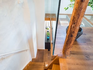 A wooden staircase with glass railings leading to a room with a plant and a basket. - Apartment  by Interhome (Zurich)
