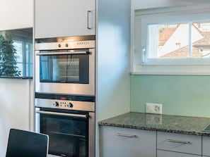 A kitchen with a built-in oven, a microwave, and a window above the countertop. - Apartment  by Interhome (Zurich)