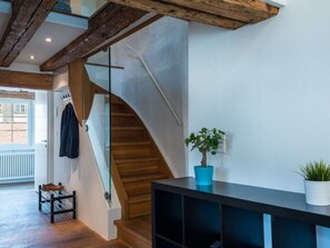 Et moderne interiør med en trappe i træ, en glasdør, en potteplante og et sort konsolbord.