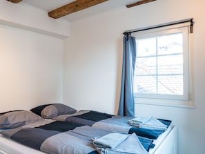 A single bed with a striped blanket and pillows, a window with a curtain, and a wooden beam ceiling. - Apartment  by Interhome (Zurich)