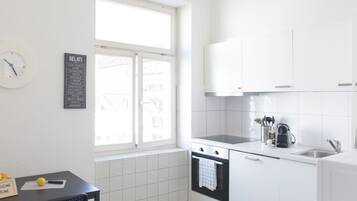 Une cuisine moderne avec des meubles blancs, une cuisinière noire et une fenêtre donnant sur les bâtiments environnants.