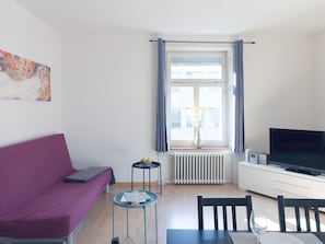Ein modernes Wohnzimmer mit einem violetten Sofa, einem Esstisch mit Stühlen, einem Fernseher und einem Fenster mit Vorhängen.