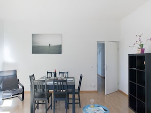 Un coin repas avec une table dressée pour deux personnes, une chaise noire et une petite table d’appoint sur laquelle se trouvent un sablier et un plateau.