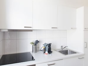 Eine moderne Küche mit weißen Schränken, einer schwarzen Induktionskochplatte, einer Kaffeemaschine und einem Spülbecken.