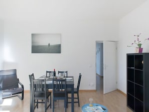 Ein Essbereich mit Tisch und Stühlen, ein Bücherregal, eine Tür zu einem anderen Raum sowie ein gerahmtes Bild an der Wand.
