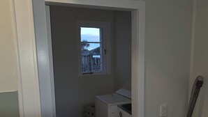 A laundry room with a washing machine, a small window, and a drying rack.