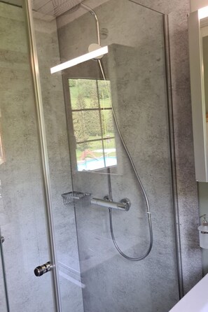 Een douche met een glazen deur, een chroomdouchekop en een metalen handgreep.