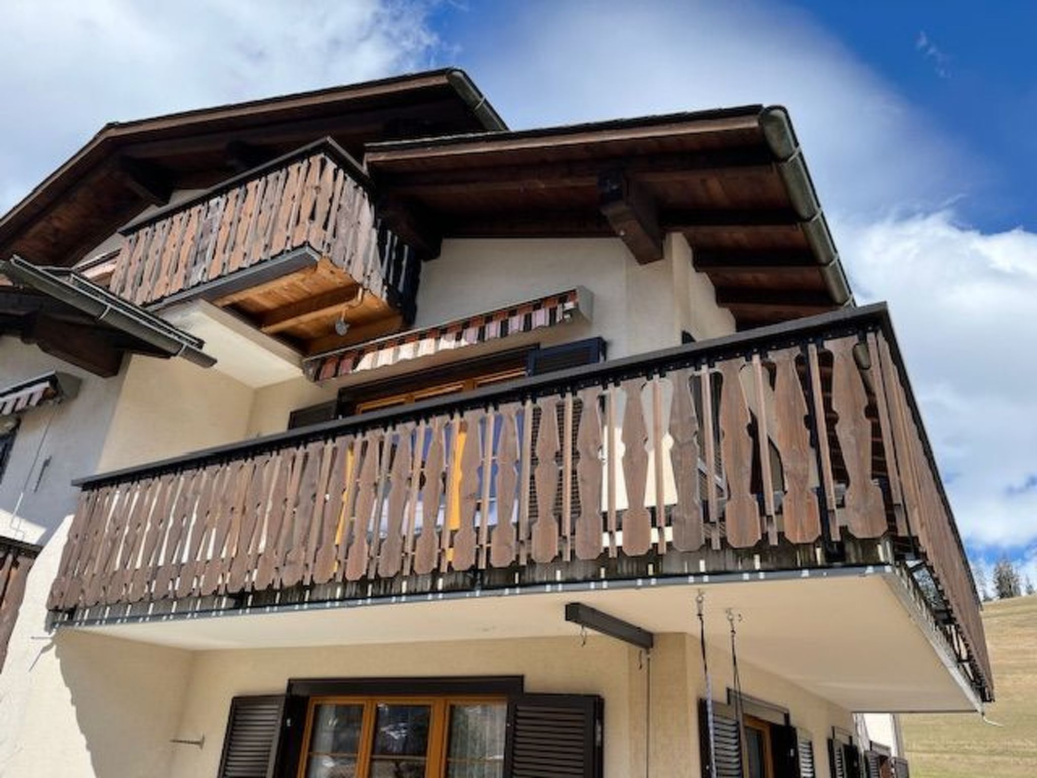 A multi-story building with a balcony featuring wooden railings and a sloped roof.