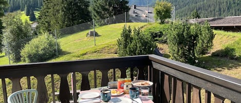 A wooden deck with a table set for a meal, overlooking a mountainous landscape.