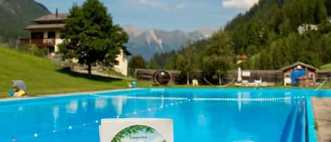 Une main tenant une carte représentant un paysage de montagne, une piscine et une montagne en arrière-plan.