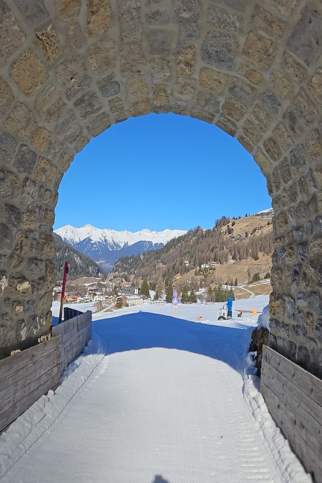 Un arco in pietra che conduce verso un paesaggio innevato sotto un cielo azzurro limpido.