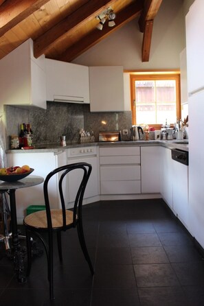 A compact kitchen with white cabinets, a granite countertop, a dining area with a round table and chairs, and a window providing natural light.
