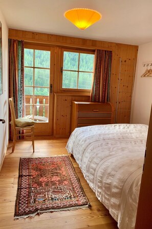 A bedroom with a bed, a chair, a desk, a window with curtains, and a hanging light fixture. - Tga Clavo°, (Filisur), 117 by Interhome (Filisur)