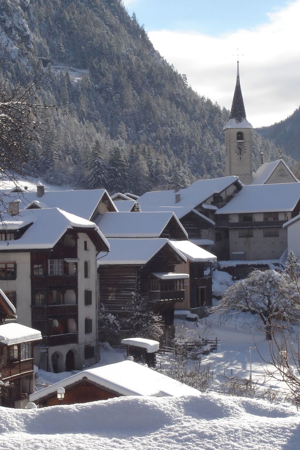 Ein verschneites Dorf mit traditionellen Holzhäusern und einem Kirchturm.