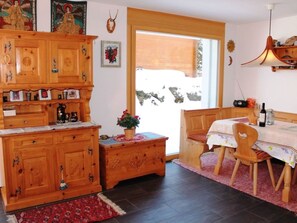 Ein Zimmer mit einem Holzkabinett, einem Esstisch mit Stühlen, einem Fenster mit Blick und einer hängenden Deckenleuchte.