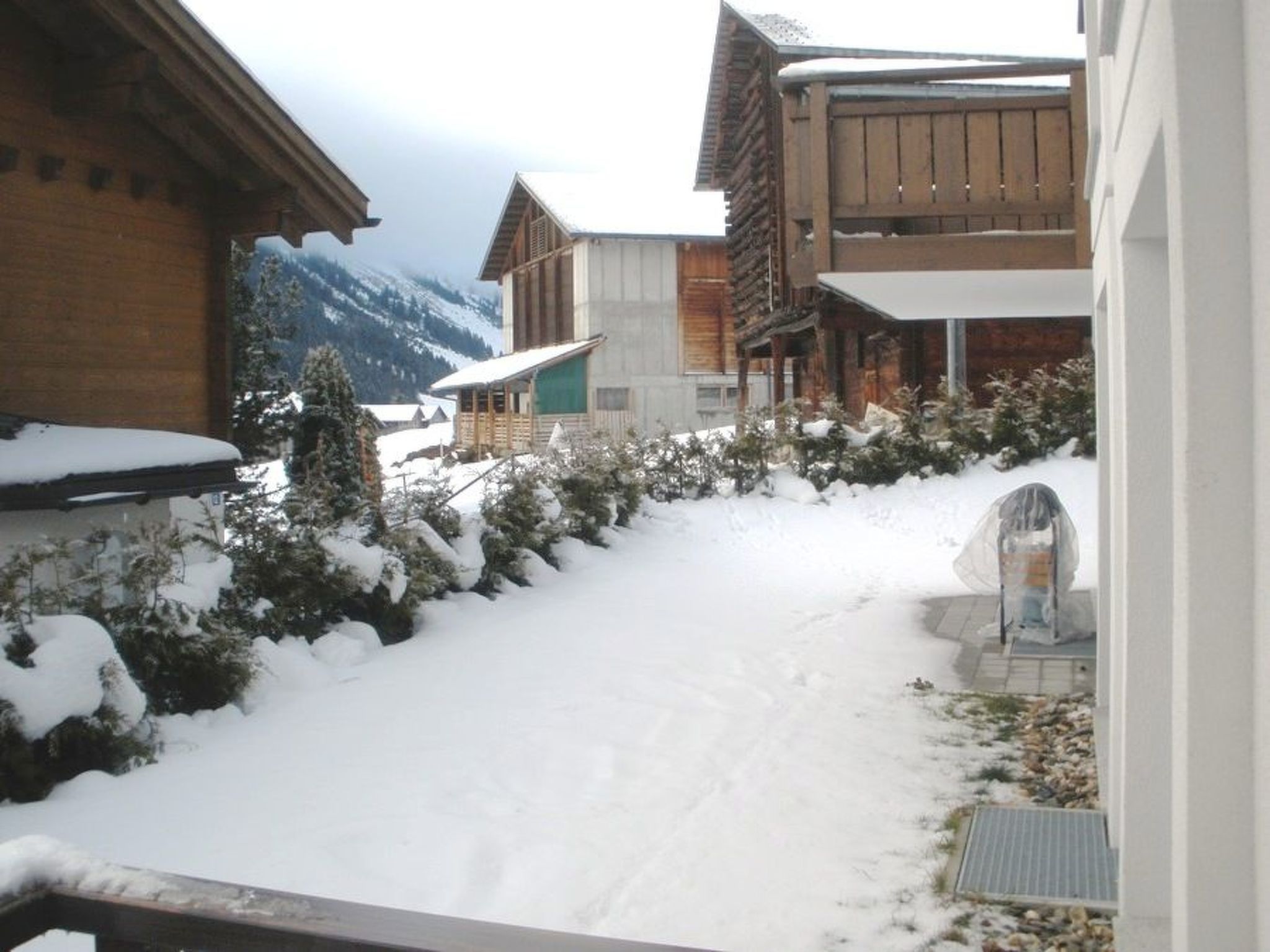 Un sentier enneigé menant à un bâtiment à la façade en bois, avec une chaîne de montagnes en arrière-plan.