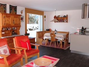 A cozy living room with a fireplace, a dining area with a table and chairs, and a kitchen area with a stove and cabinets. - Huggel, (Camischolas/Sedrun), 228.01 by Interhome (Camischolas)