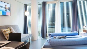 Une chambre d’hôtel avec un lit, un bureau avec un ordinateur portable, un canapé et une grande fenêtre avec des rideaux.