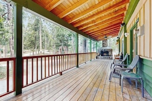 Ein überdachter Balkon mit Holzboden, einem Kamin aus Stein und Blick auf einen Wald.