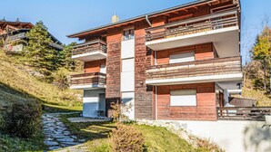 Ein modernes, zweistöckiges Haus mit Natursteinfassade, mehreren Balkonen und einem Kiesweg, der zum Eingang führt.