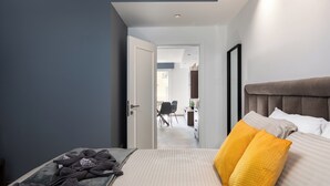 A hotel room with a bed, a bedside table, a headboard, and a door leading to a hallway. - Modern 1BR APTS near Manoel & Tigne (Gżira)