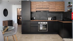 A modern kitchen with dark cabinetry, a built-in oven, and a dining area with a glass table and chairs. - Modern 1BR APTS near Manoel & Tigne (Gżira)