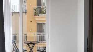 A modern room with a glass table, chairs, a sofa, a sliding glass door to an outdoor balcony, and a view of a building with balconies. - Modern 1BR APTS near Manoel & Tigne (Gżira)