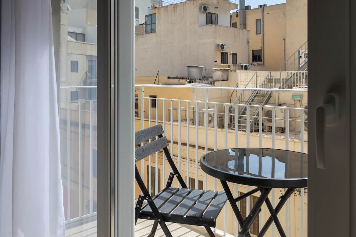 Un balcon avec une table et des chaises, une vue sur les immeubles et un ciel dégagé.