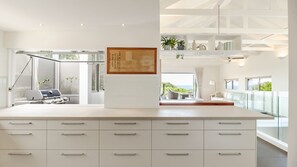 A modern kitchen with a central island, a dining area with a view, and a living space with a balcony. - Aqua North House – Ocean Views & Pool (Sunshine Beach)