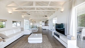 A spacious living area with a white sofa, a coffee table, a TV, and a balcony with a view. - Aqua North House – Ocean Views & Pool (Sunshine Beach)