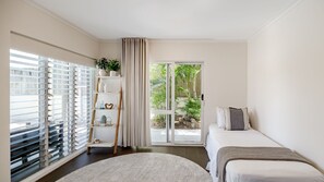 A bedroom with a bed, a window with blinds, a plant, and a view of greenery outside. - Aqua North House – Ocean Views & Pool (Sunshine Beach)
