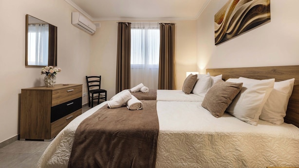 A hotel room with two beds, a wooden dresser, a chair, a mirror, and a painting on the wall. - Luxury 1BR Stay at The Podium - Marina (Msida)